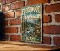 A vintage-style metal sign for the Floodwood State Forest in Idaho, featuring a scenic illustration of a forest and a river.