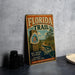 A vintage metal sign advertising the Florida Trail, featuring a scenic illustration of a forest and a road, is displayed on a gray concrete surface.