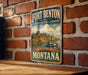 A vintage-style metal sign for Fort Benton National Historic Landmark in Montana, featuring an illustration of a castle and a river.