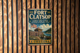 A vintage-style metal sign for Fort Clatsop, Lewis and Clark National Historical Park, with an American flag and a wooden fence in the background.