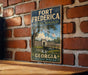 A vintage-style metal sign for Fort Frederick, a National Monument in Georgia, featuring a scenic image of the fort and its surroundings.