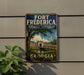 A vintage-style metal sign for Fort Frederick National Monument in Georgia, featuring a scenic illustration of the monument surrounded by a bridge and palm trees.