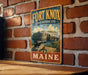 A vintage-style metal sign for the Fort Knox State Historic Site in Maine, featuring an illustration of a cannon and a building, mounted on a brick wall.