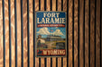 A vintage-style sign for the Fort Laramie National Historic Site in Wyoming, featuring an illustration of a building and a wagon.