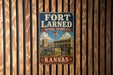 A vintage-style metal sign for the Fort Larned National Historic Site in Kansas, featuring an image of a cannon and a building.