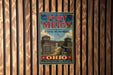 A vintage-style metal sign for the Fort Meigs State Memorial, featuring a cannon and a wooden fortification, is displayed on a wooden wall.
