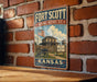 A vintage-style metal sign for the Fort Scott Historic Site in Kansas, featuring an illustration of a historic building and a cannon.