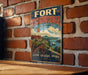 A vintage-style metal sign with the text "FORT TICONDEROGA NEW YORK" and an illustration of a fort, ship, and landscape, hanging on a brick wall.