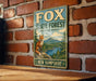 A vintage metal sign for Fox State Forest in New Hampshire, featuring an illustration of a fox in a forest setting.
