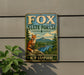 A metal sign with a fox sitting on a rock, surrounded by a forest landscape, is mounted on a wall.
