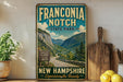 a vintage-style sign for Franconia Notch State Park, with a scenic mountain landscape in the background.