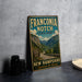 A vintage-style metal sign for Franconia Notch State Park, featuring a scenic mountain landscape and the text "Franconia Notch State Park" prominently displayed.