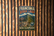 A vintage metal sign for the Franconia Ridge Loop trail in New Hampshire, featuring a mountain landscape and trail information.