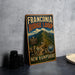 A vintage-style metal sign for the Franconia Ridge Loop trail in New Hampshire, featuring a mountain landscape and trail markers.