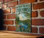 A vintage metal sign for the Freetown-Fall River State Forest in Massachusetts, featuring a scenic illustration of a forest and a river.