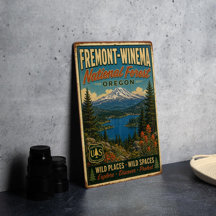 a vintage metal sign for the Fremont-Winebra National Forest in Oregon, with a mountain landscape and a lake in the background.