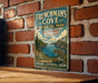 A vintage-style metal sign for "Frenchman's Cove" in Nova Scotia, Canada, mounted on a brick wall.