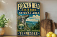 A vintage-style sign for Frozen Head State Park and the Natural Area in Tennessee, featuring a scenic mountain landscape with pine trees and a waterfall.