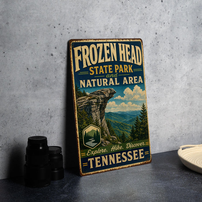 A vintage-style metal sign for Frozen Head State Park in Tennessee, featuring a scenic mountain landscape and the text "FROZEN HEAD STATE PARK NATURAL AREA EXPLORE, HIKES, DISCOVER TENNESSEE".