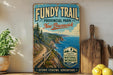 a vintage-style sign for the Fundy Trail in New Brunswick, New Brunswick, Canada, with a scenic coastal landscape and a wooden paddleboard.
