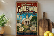 a vintage-style metal sign that reads "Welcome to GAINESWOOD ALABAMA" with a picture of a town and a clock tower. The sign also includes the words "Small Town Big Heart" and "History, Community, Home" below the image.
