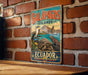 A vintage-style metal sign with the text "GALAPAGOS ISLANDS ECUADOR" and an illustration of various animals, including a bird, a turtle, and a lizard, set against a backdrop of a mountain and a body of water.