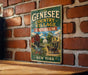 A vintage-style metal sign for the Genesee Country Village & Museum in New York, featuring an illustration of a rural scene with a horse-drawn carriage and a red brick building.