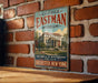 A vintage metal sign for the George Eastman Museum in Rochester, New York, featuring an illustration of the museum's building and surrounded by trees.