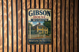 A vintage metal sign for the Gibson House Museum in Massachusetts, featuring an illustration of a yellow house with a white picket fence and a blue sky with clouds.