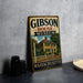 A vintage metal sign for the Gibson House Museum in Massachusetts, featuring an illustration of a yellow house with a white picket fence and a blue sky with clouds.