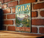 A vintage-style metal sign for the Gila National Forest in New Mexico, featuring a scenic mountain landscape and text promoting the area's natural beauty and outdoor activities.