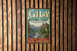 A vintage metal sign for Gila National Forest in New Mexico, featuring a scenic landscape with mountains, trees, and a river.
