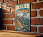A vintage-style metal sign for Glacier National Park, specifically the Highline Trail, is displayed on a brick wall.