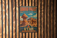 A vintage-style metal sign for Goblin Valley State Park, featuring a desert landscape with a mushroom-shaped formation, mounted on a wooden wall.
