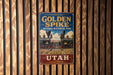 A vintage-style sign for Golden Spike National Historical Park in Utah, featuring an illustration of a train and mountains.
