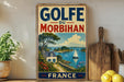 A vintage-style sign for Golfe du Morbihan, a French island, featuring a scenic landscape with a house, sailboat, and blue sky.