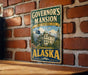 A vintage-style metal sign displaying the name "Governor's mansion" and the state of Alaska, mounted on a brick wall.
