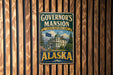 A vintage metal sign for Governor's mansion in Alaska, featuring a large building and a flag.