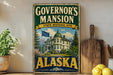 A vintage-style metal sign for Governor's mansion in Alaska, featuring a large image of the mansion and the state's flag.