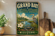 A vintage-style metal sign for the Grand Bay National Estuarine Research Reserve in Mississippi, featuring an illustration of a heron, a crab, and a flower.