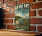 A vintage-style metal sign for the Grand Bay National Estuarine Research Reserve in Mississippi, featuring an illustration of a bird, flowers, and a body of water.
