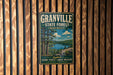 A vintage metal sign for Granville State Forest in Massachusetts, featuring a scenic landscape with pine trees, a lake, and mountains.