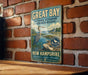 A vintage-style metal sign for the Great Bay National Estuarine Research Reserve in New Hampshire, featuring an illustration of a heron and a coastal landscape.