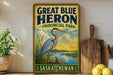 A vintage-style sign for "Great Blue Heron Provincial Park" in Saskatoon, featuring an illustration of a heron standing on a grassy bank overlooking a river.