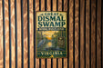 A vintage-style metal sign for the Great Dismal Swamp National Wildlife Refuge in Virginia, featuring an illustration of a bird and a swampy landscape.