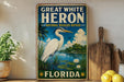 A vintage-style sign for the Great White Heron National Wildlife Refuge in Florida, featuring an illustration of a heron standing on a pond surrounded by palm trees and other natural elements.