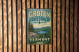 A vintage metal sign for Groton State Forest in Vermont, featuring a scenic landscape with pine trees, mountains, and a lake.