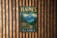 A vintage metal sign for Haines State Forest in Alaska, featuring a scenic mountain landscape and a road leading through the forest.