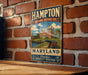 A vintage metal sign for the Hampton National Historic Site in Maryland, featuring an illustration of a historic building and a cannon, mounted on a brick wall.