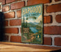 A vintage-style metal sign for the Hapgood State Forest in Vermont, featuring a scenic landscape with a lake and mountains.